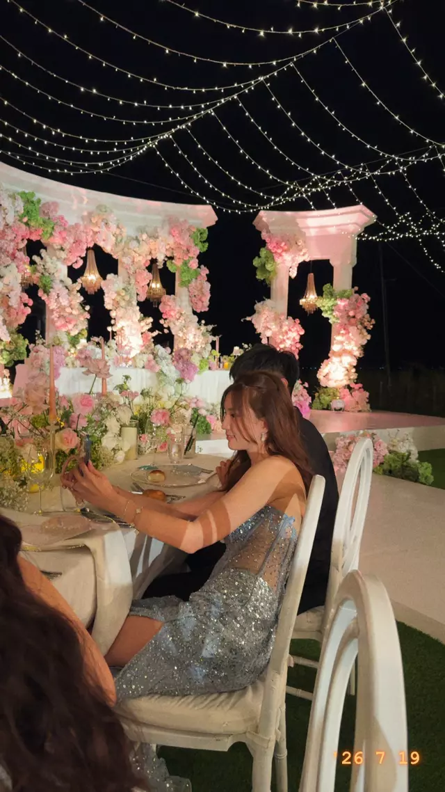 A candlelit dinner table under fairy lights and pink flowers